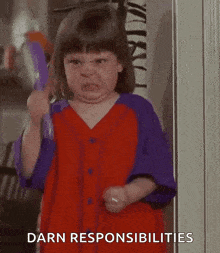 a little girl in a red and purple dress is holding a brush and making a face .