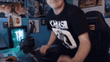 a man in a black t-shirt is sitting in a chair in a room .