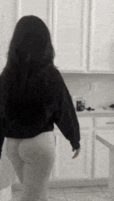 a woman in a black shirt and white pants is standing in a kitchen