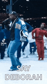 a man is singing into a microphone while a group of people are dancing behind him .