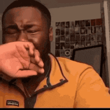 a man in a yellow jacket is covering his face with his hand .