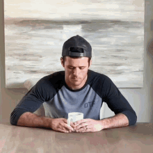 a man wearing a baseball cap and a shirt that says otf sits at a table with a cup of coffee