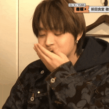 a person covering their mouth with their hand with ej / k / yuma on the bottom right