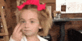 a little girl with a red bow in her hair is making a face .