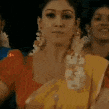 a woman in a yellow saree and a red top is standing in front of a crowd of people .