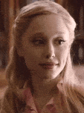 a close up of a woman 's face with blonde hair and a pink shirt