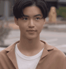 a young man in a brown shirt and white t-shirt looks at the camera