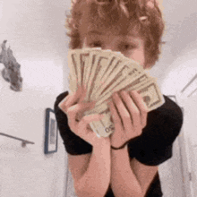 a young boy is holding a fan of money in front of his face .