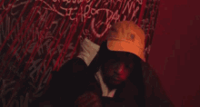 a man wearing a yellow carhartt hat stands in front of a wall with graffiti