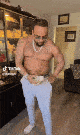 a shirtless man is standing in a living room with his hands in his pockets and a tiktok sticker