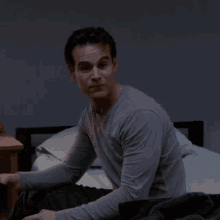 a man in a grey shirt is sitting on a bed looking at something