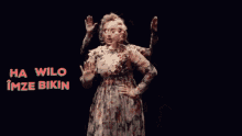 a woman in a floral dress stands in front of a sign that says ha wilo imza bikin