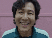 a close up of a man 's face smiling in front of a pink wall